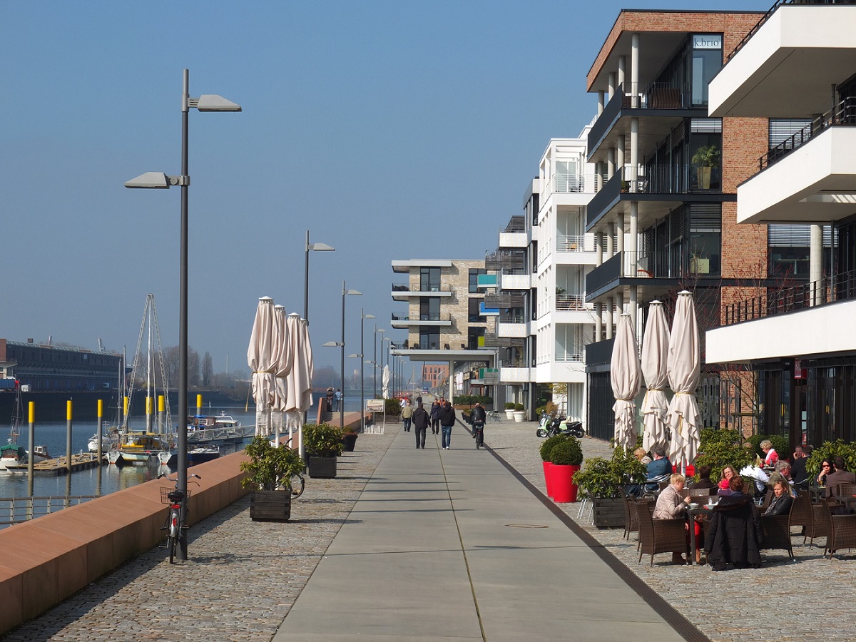 Promenade mit flanierenden Menschen, links Fluss Weser, rechts Gebaeude und Terassen